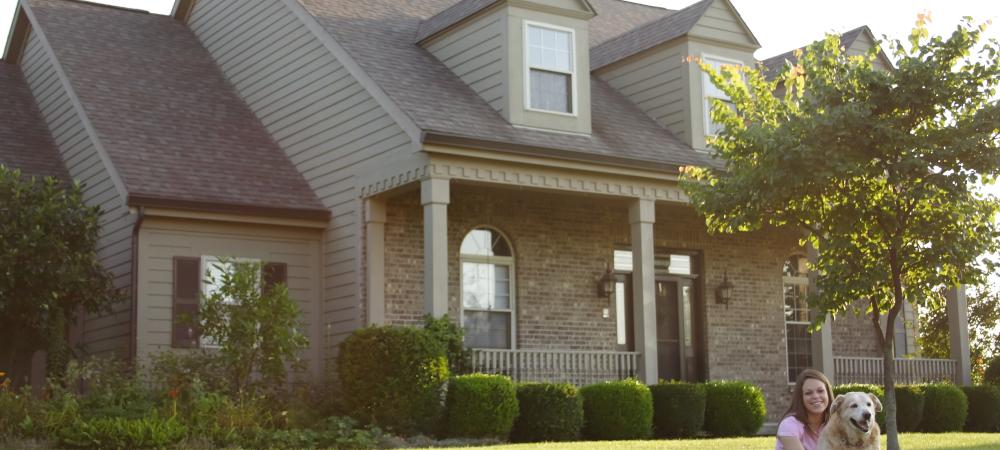 woman sitting on her large lawn with her dog next to her in front of their home